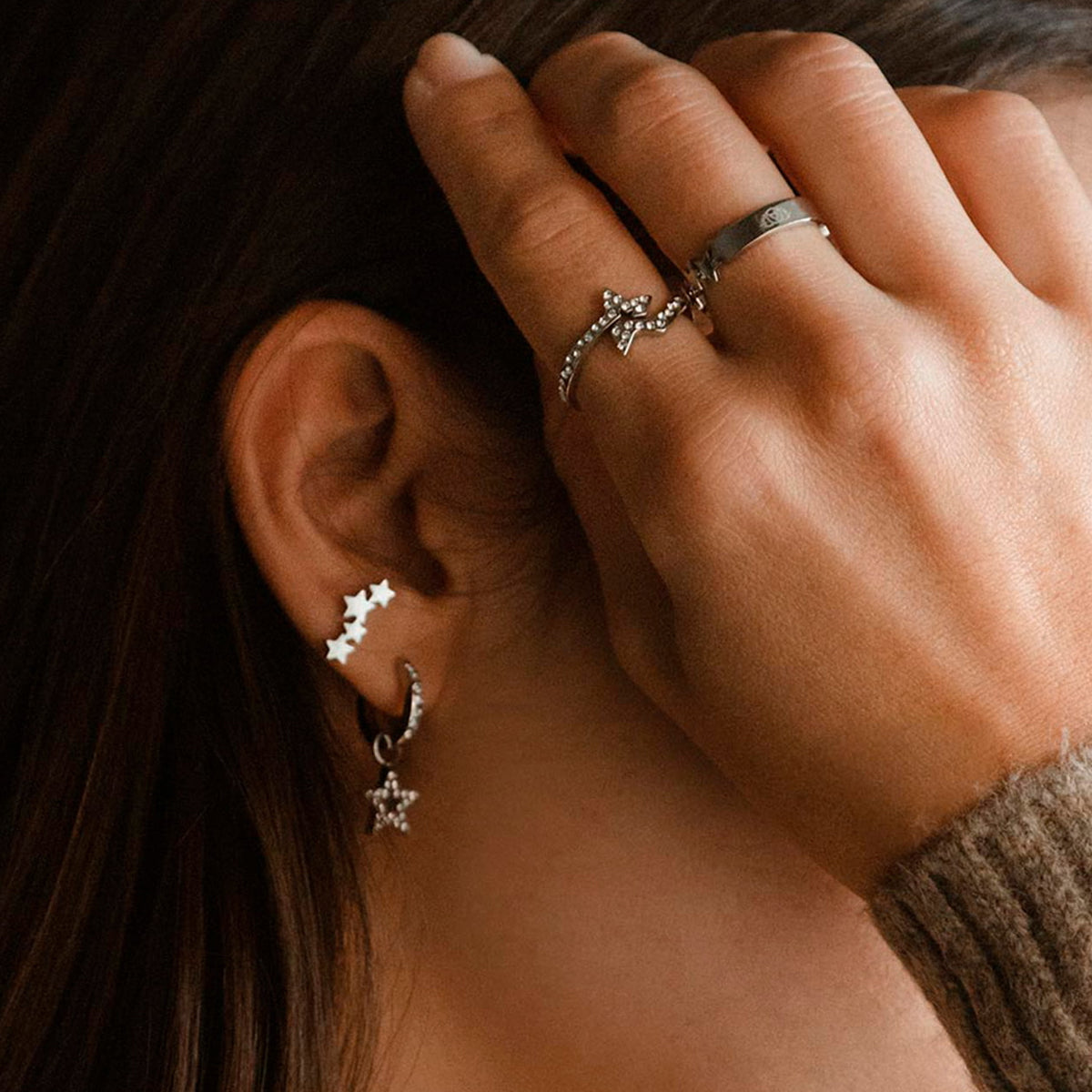Woman wearing AN JEWELS JEWELRY Mod. ADC.R02S-8 star earrings and rings in a cozy setting.