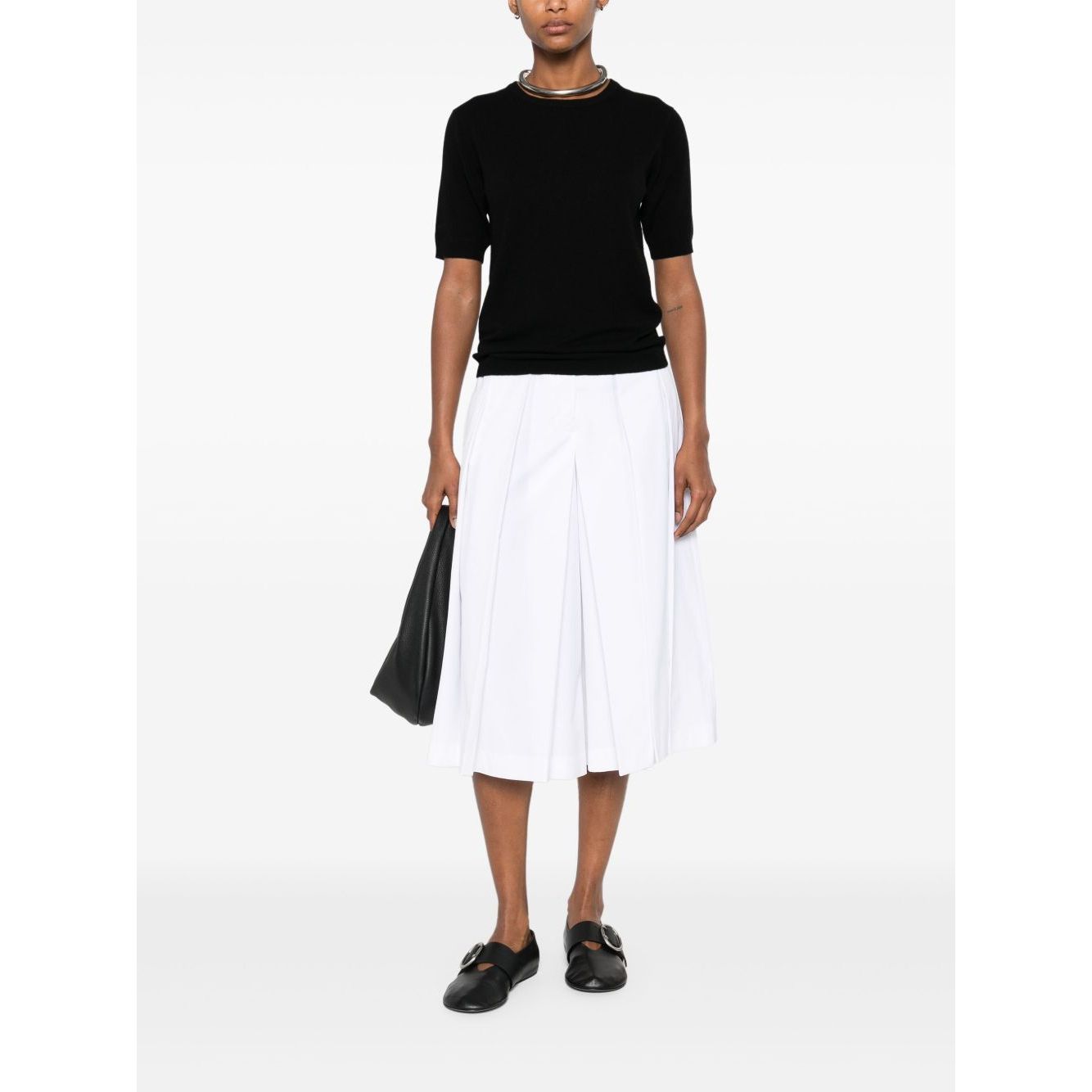 Woman wearing SOFT GOAT Sweaters Black cashmere crewneck top with short sleeves, styled with a white pleated skirt and black shoes.