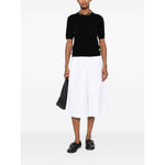 Woman wearing SOFT GOAT Sweaters Black cashmere crewneck top with short sleeves, styled with a white pleated skirt and black shoes.
