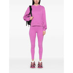 Woman wearing Adidas By Stella McCartney Trousers Purple with logo and elastic waistband, standing in pink outfit and sneakers.