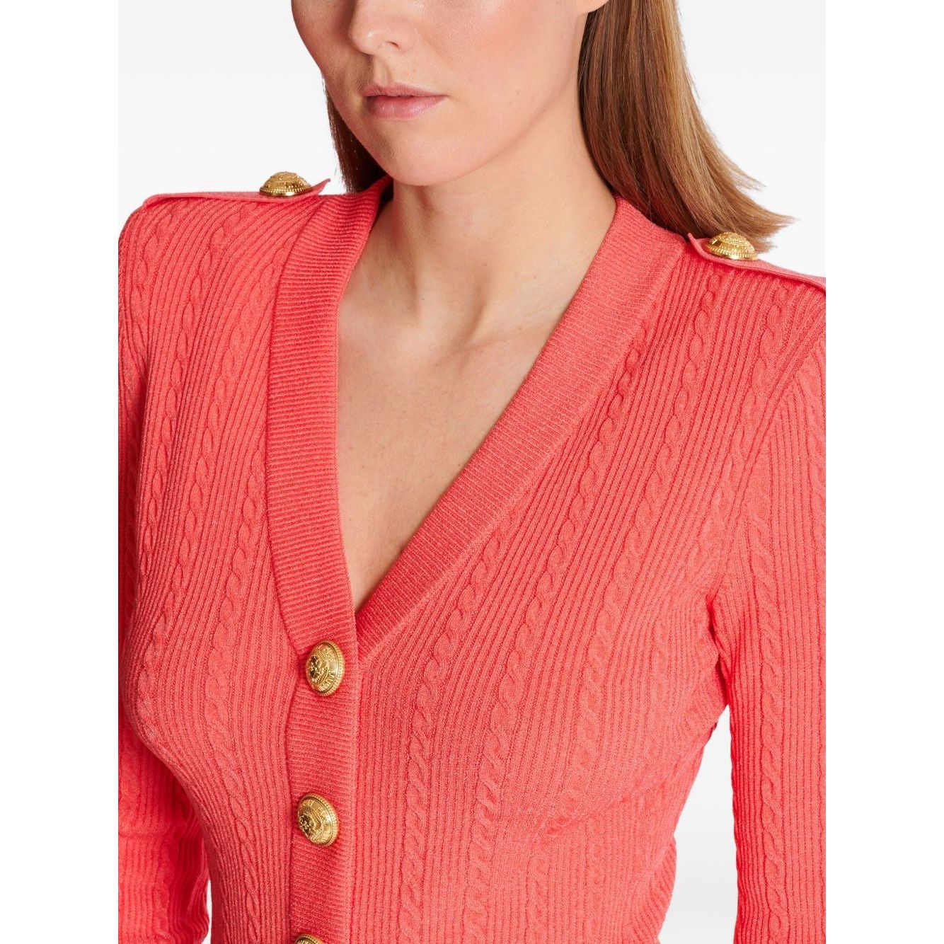 Balmain Long-sleeved twisted knit cardigan in coral pink with logo-embossed buttons and epaulettes, showing a close-up of the V-neck style.