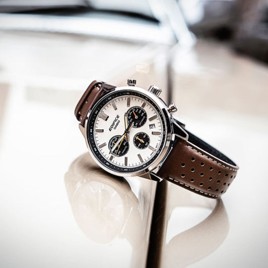 CASIO EDIFICE Mod. STANDARD CHRONOGRAPH - CHAMPAGNE with brown leather strap on reflective surface showcasing luxury design.