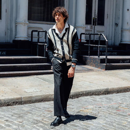 Man wearing a stylish black and white outfit walking on a cobblestone street.
