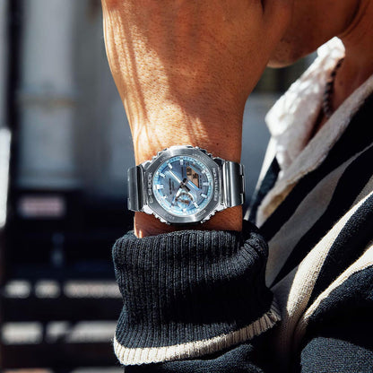 Person wearing CASIO MOD. GM-2110D-2AER watch, silver design, outdoor setting.