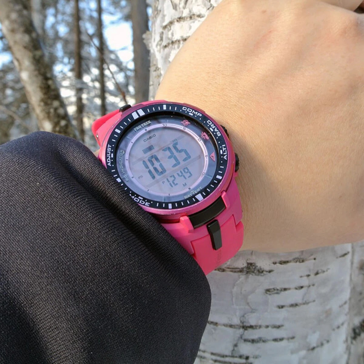Person wearing CASIO PRO TREK - THOUGH SOLAR - TRIPLE SENSOR wristwatch with pink resin strap, shown outdoors.