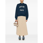 Model wearing Chloé Chloè Sweaters Blue with logo patch, mock neck, long sleeves, paired with beige skirt, holding a Chloé handbag.