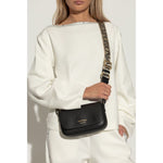 Woman wearing Emporio Armani Crossbody mini bag with black logo-print strap and gold-tone hardware on white outfit.