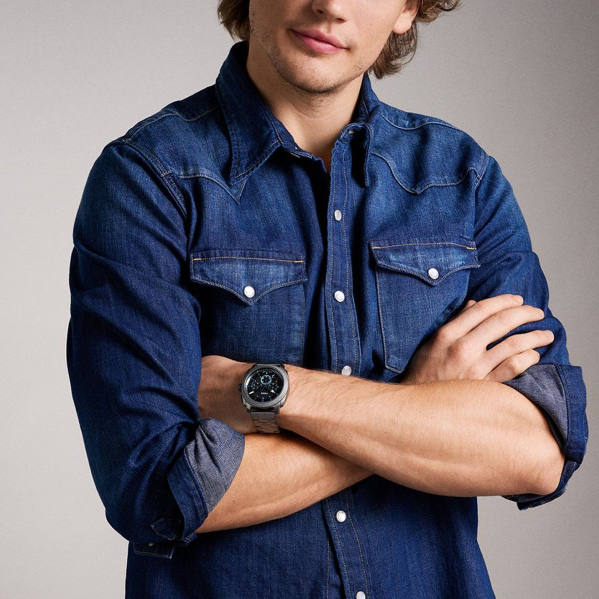 Man wearing FOSSIL Mod. MACHINE wristwatch, 44mm case, on wrist, crossing arms, denim shirt, official box packaging included, Gent's watch.