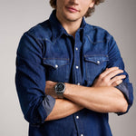 Man wearing FOSSIL Mod. MACHINE wristwatch, 44mm case, on wrist, crossing arms, denim shirt, official box packaging included, Gent's watch.