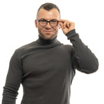 Person wearing glasses and a dark turtleneck, adjusting frames with a smile.
