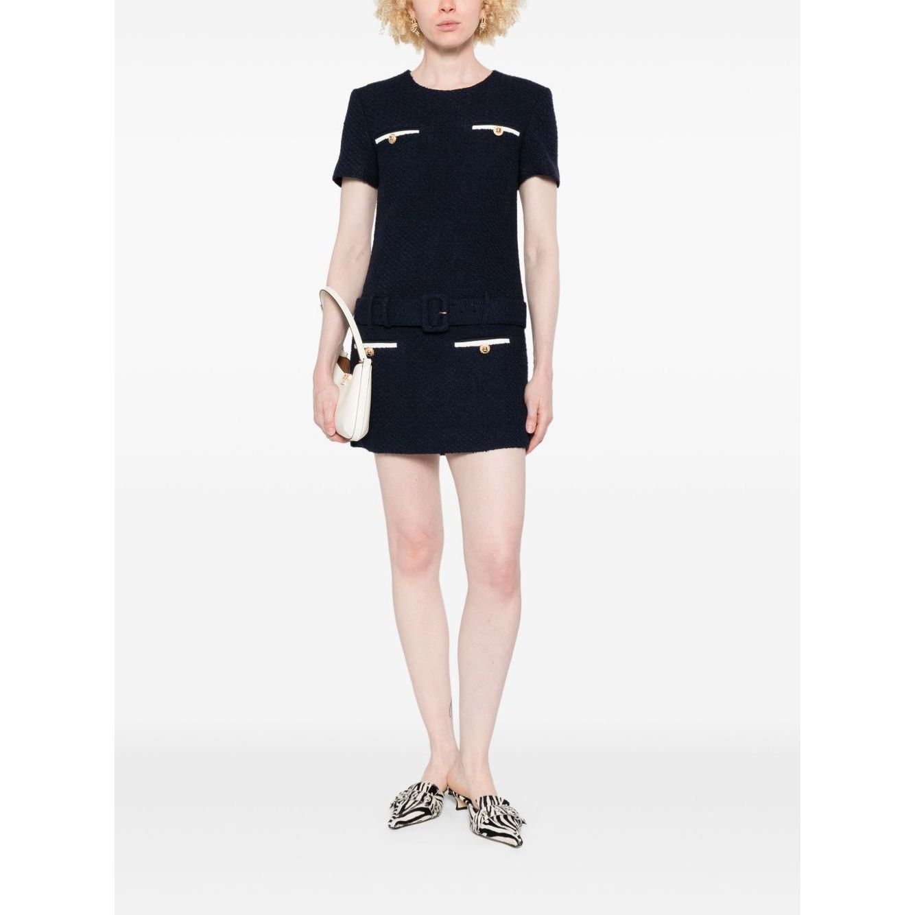 Model wearing Self-portrait Dresses Blue navy boucle mini dress with belt, welt pockets, and concealed zip, holding a white clutch.