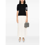 Person wearing navy Thom Browne Sweaters Blue with 4Bar wool design and grosgrain tab, paired with a white skirt and holding a gray handbag.