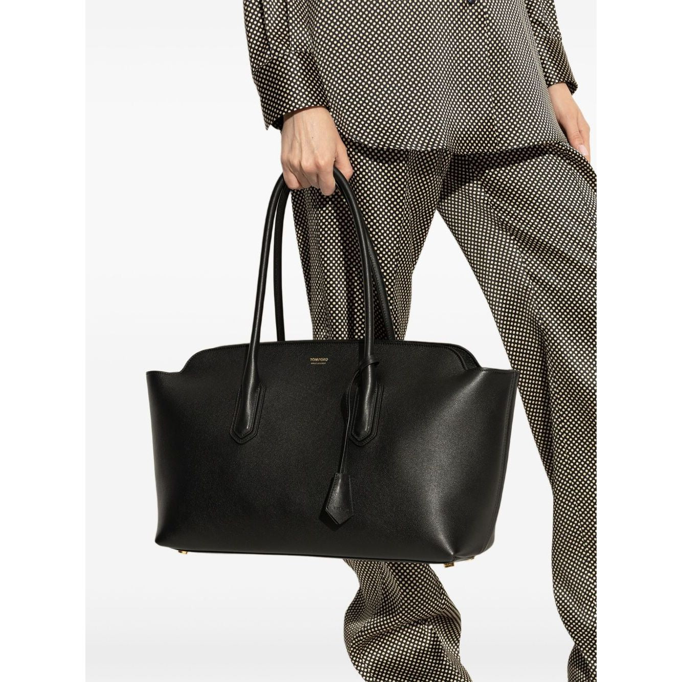 Tom Ford Structured Tote Bag in black smooth leather with dual top handles, stylishly held by a person wearing a checkered outfit.
