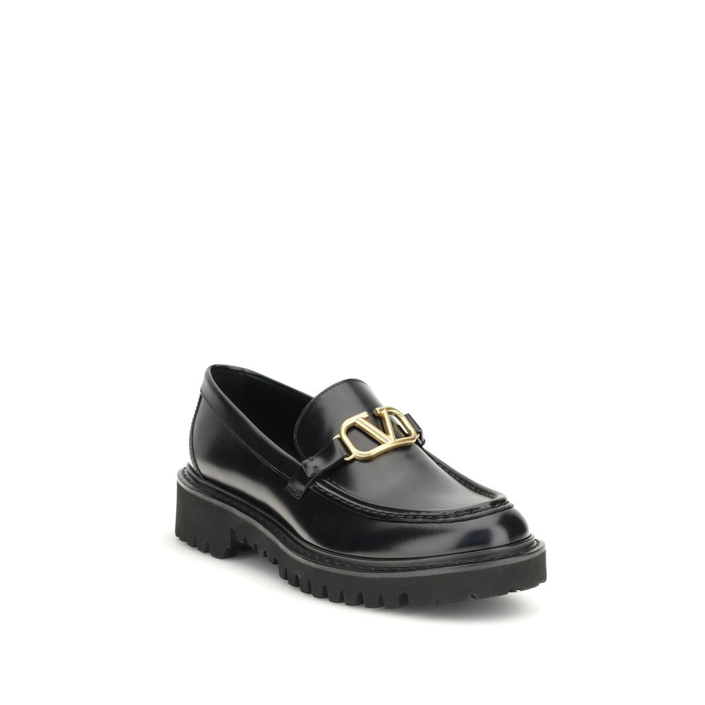 Valentino Garavani Black Leather Slip-On Loafers with brass VLogo and rubber lug sole, showcasing classic and contemporary style.